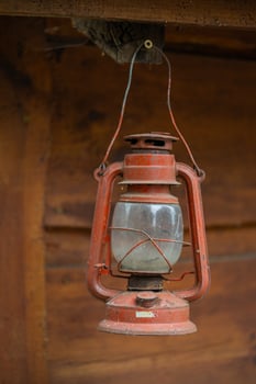 Vintage red kerosene lantern hanging on a wooden beam, showcasing rustic charm and nostalgia. Concept of retro lighting, antique decor, and old-fashioned outdoor gear photo