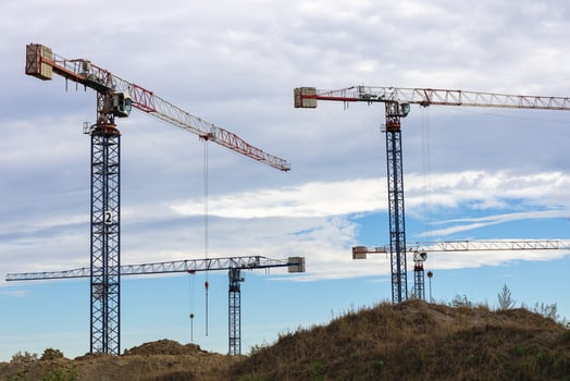 Tower cranes at a construction site against a cloudy sky and grassy terrain on a sunny day. Concept of urban development, building infrastructure, and industrial construction photo