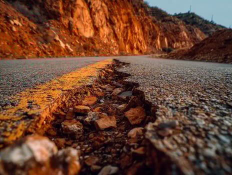 Close-up of a cracked mountain road with rocky debris and rugged cliffs in the background photo