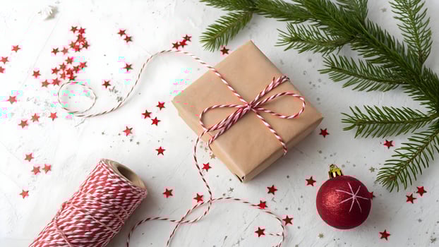 Festive Christmas Gift Wrapping Scene Brown Paper Gift Box Tied with Red and White String, Ornament, Star Confetti, and Pine Branch on White Background photo