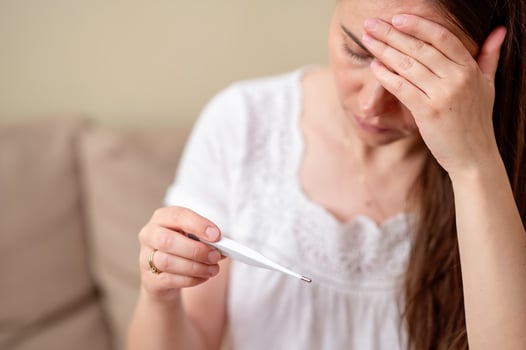 Tired woman holding her head, looking at thermometer while measuring temperature photo