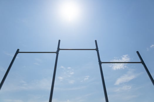 Metal scaffolding stands against a clear blue sky with sunlight illuminating the scene and soft white clouds in the background photo