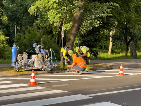 Construction workers in safety gear fix a crosswalk surrounded by trees in a peaceful park during the early evening photo