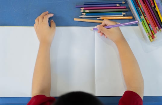 Top view of small child draws with pencil and color on white notebook with copy space. photo