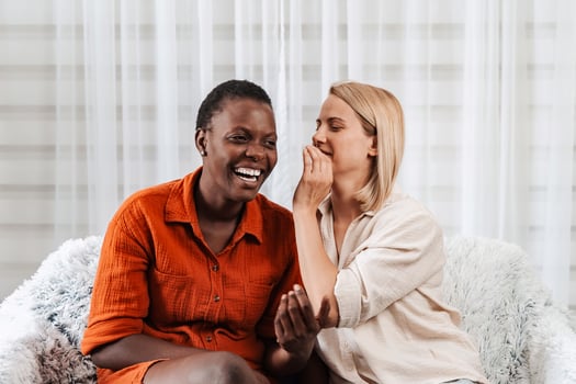 Two young women whispering secrets and laughing on the sofa photo