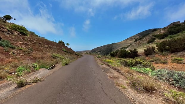 A Scenic Road Winding Through Lush Green Hills Underneath a Bright Blue Sky Above photo