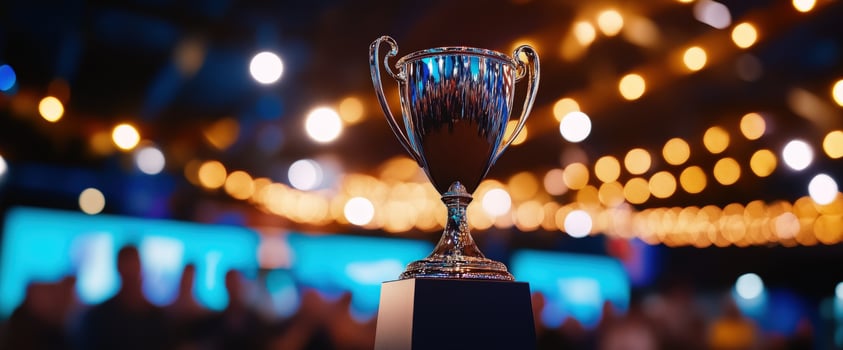 A gleaming trophy stands tall, a symbol of triumph and achievement, bathed in the warm glow of celebratory lights. The blurred background hints at a vibrant event. photo