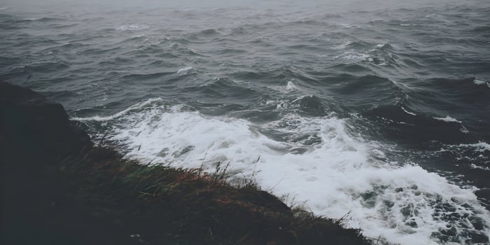 Ocean waves crashing against a rocky cliff on a cloudy day photo