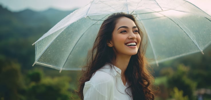 The woman smiling under a transparent umbrella in a serene natural landscape. photo