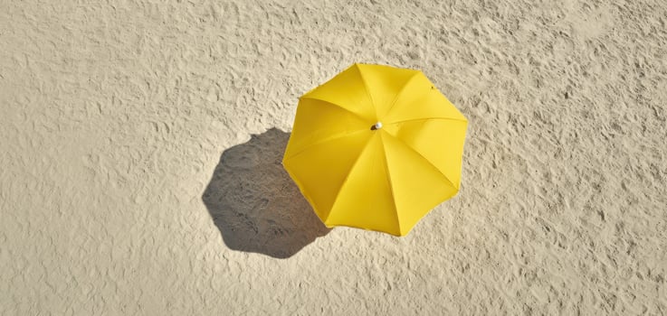 The vibrant yellow umbrella casting a shadow on sandy beach. photo