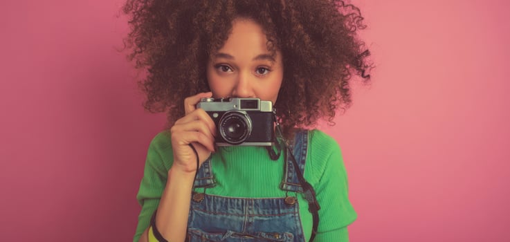 The young woman with a camera exuding creativity against a vibrant pink backdrop. photo