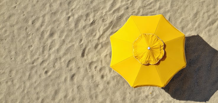 The Bright Yellow Umbrella Casting a Shadow on Sandy Beach photo