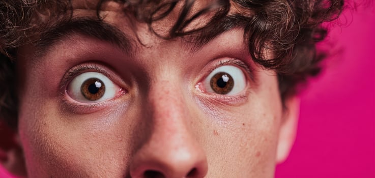 The surprised young man showcasing wide eyes against a vibrant pink background. photo