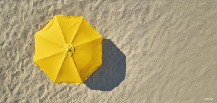 The bright yellow umbrella casting a shadow on the sandy beach. photo