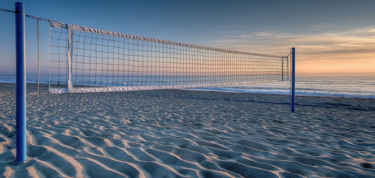 The beach volleyball net standing against a serene sunset over the ocean. photo