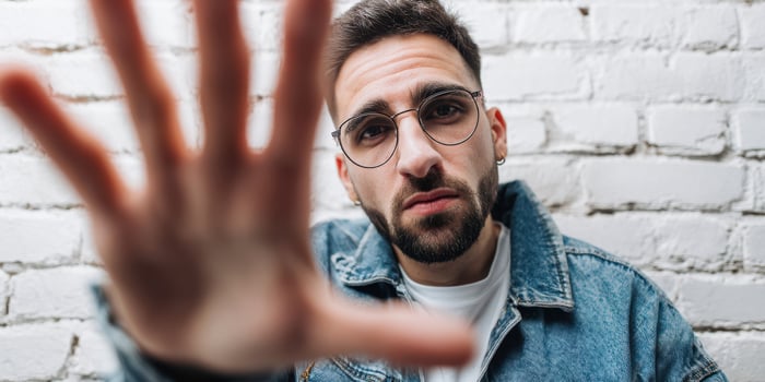 The man in glasses expressing emotion against a textured white brick wall. photo