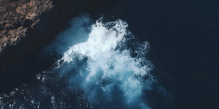 Ocean wave crashing against dark rocks from above photo