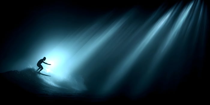 Surfer riding a wave in dark ocean water with light rays photo