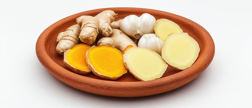 Fresh turmeric root, ginger slices, and garlic bulbs on rustic clay plate with bright colors photo