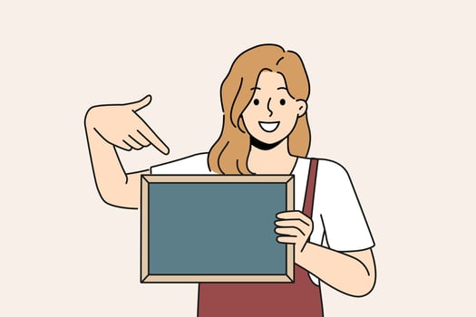 Woman waiter is holding chalkboard with copy space for drawing menu or promotional offers from restaurant. Cheerful girl waiter in apron points with finger at place for name of bar or cafe logo vector