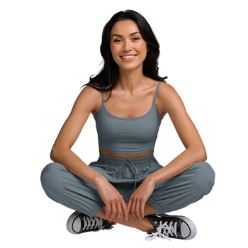 young woman in a gray athletic ensemble is sitting on the floor with her legs crossed smiling at the camera on transparent background png