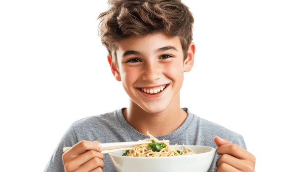 A teenage boy joyfully slurping delicious noodles from a bowl while sitting at a table, perfect for showcasing casual dining experiences or food culture imagery.. png
