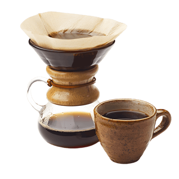 A coffee cup sits next to a coffee filter and a glass carafe png