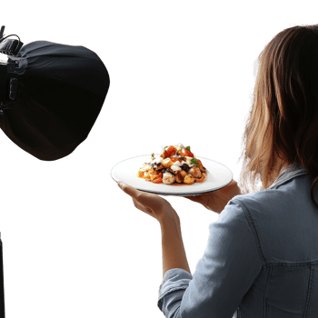 A woman holds a beautifully plated dish while a camera captures the moment. png