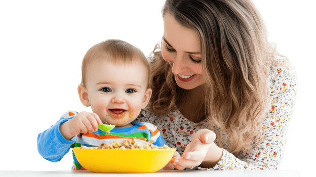 Smiling baby enjoys a meal while sitting at a table with mother in a bright indoor setting during the day png