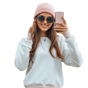 A casual woman wearing a pink beanie smiles while taking selfies with her phone outdoors on a sunny day, Casual woman taking pictures with her phone file no background png