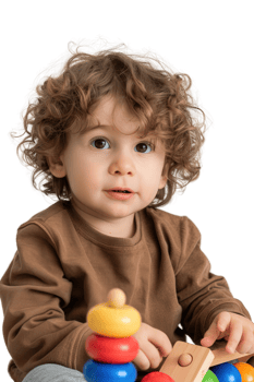 Cute child with curly hair playing with colorful toy blocks while sitting on a soft surface in a bright and cheerful environment png