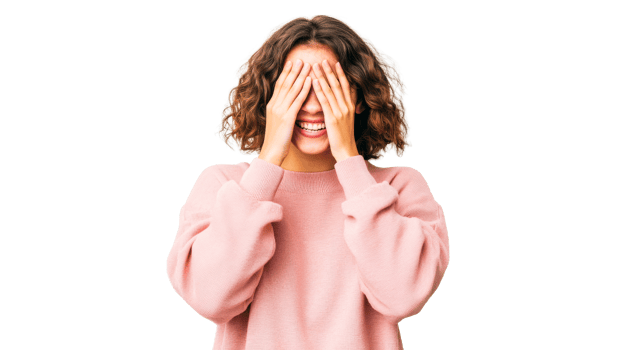 Brunette woman hides face with hands, smiling against black, cut out transparent png