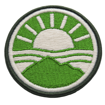 Round embroidered patch features stylized sun rising over green mountain landscape, with rays extending outward. design is simple and vibrant, using green and white thread to create natural png