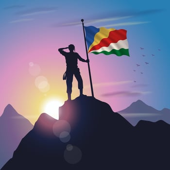 Seychelles flag raised on mountain peak with purplish yellow sunset background vector