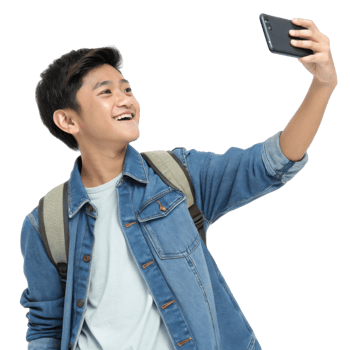 Teen boy taking selfie with smartphone, smiling, wearing denim jacket and backpack, cheerful expression, modern lifestyle, technology use png