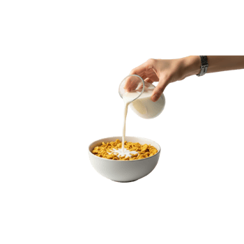 A hand is pouring milk from a glass into a white bowl filled with crunchy cereal for a png