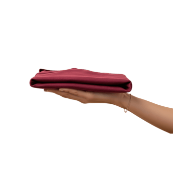 A persons hand holds a neatly folded dark red longsleeved shirt against a plain png