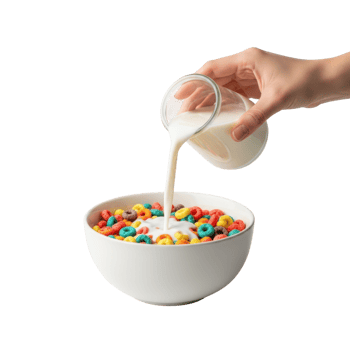 A hand pours milk from a glass jug into a white bowl filled with colorful crunchy png